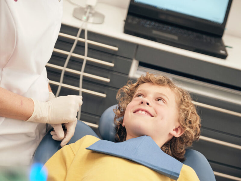 Adult woman in doctor uniform speaking to little patient in dentist office